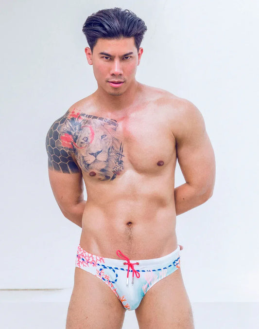 A person wears white printed swim briefs with a coral, blue, and red nautical pattern and a bright pink drawstring.