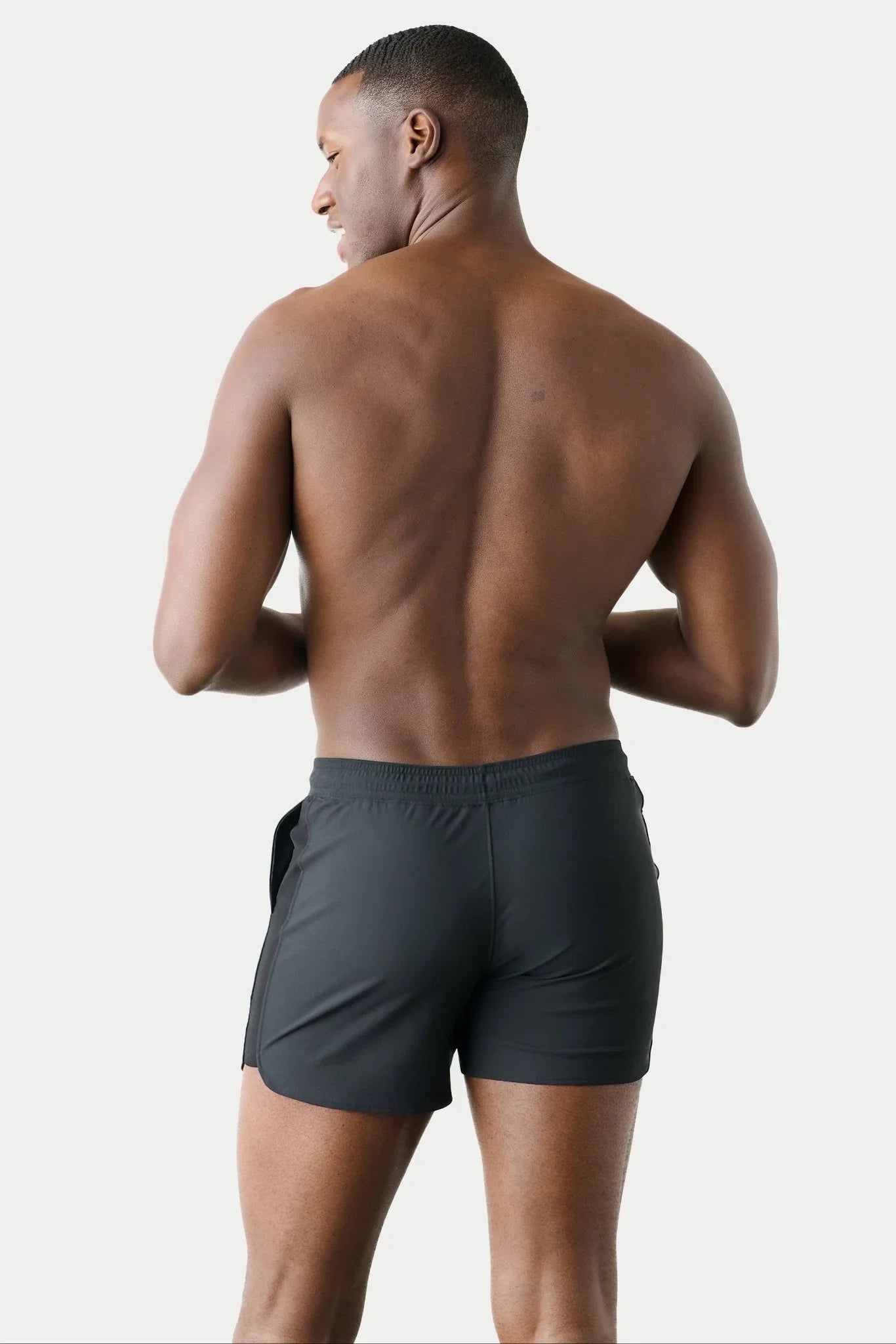 Rear view of a man wearing black AWRY Edge gym shorts against a white background.