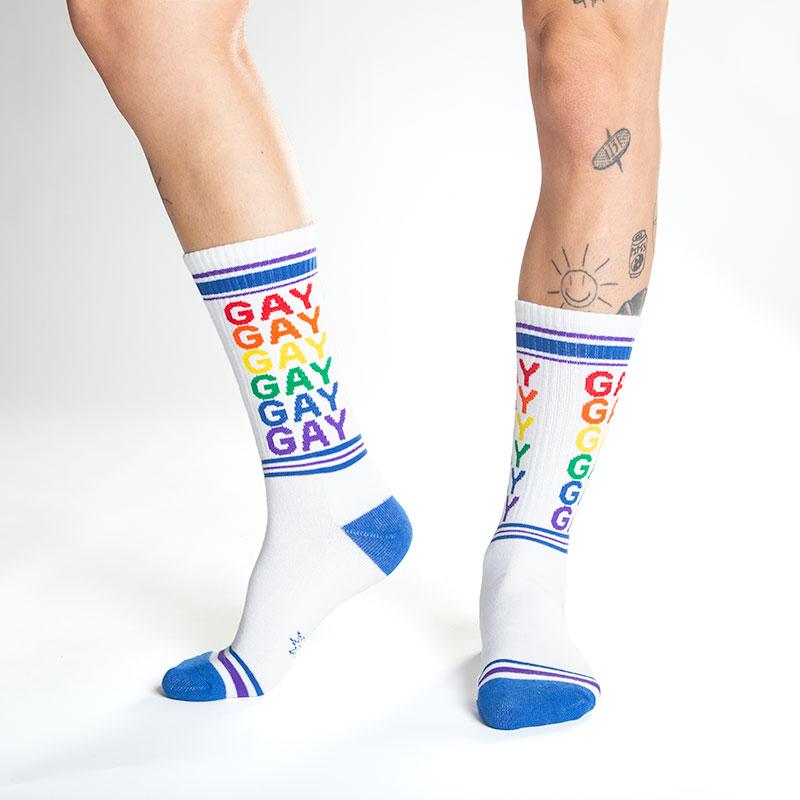 White crew socks with rainbow colored gay text and blue toe heel and cuff accents for pride wear