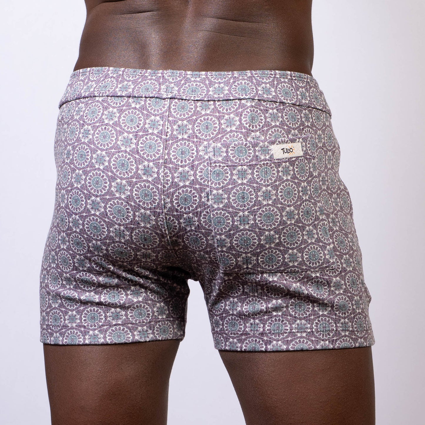 Back side of gray and white mandala linen texture shorts with a circular pattern and brand tag on the waistband