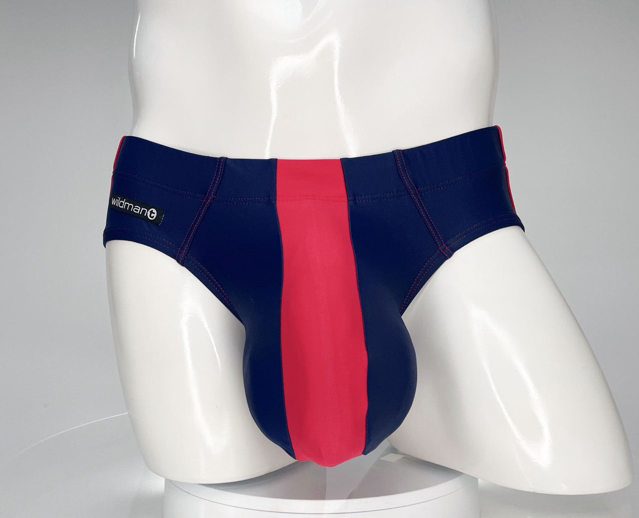 WildmanT navy and red swim brief with a prominent center red panel and white branded tag on a mannequin.