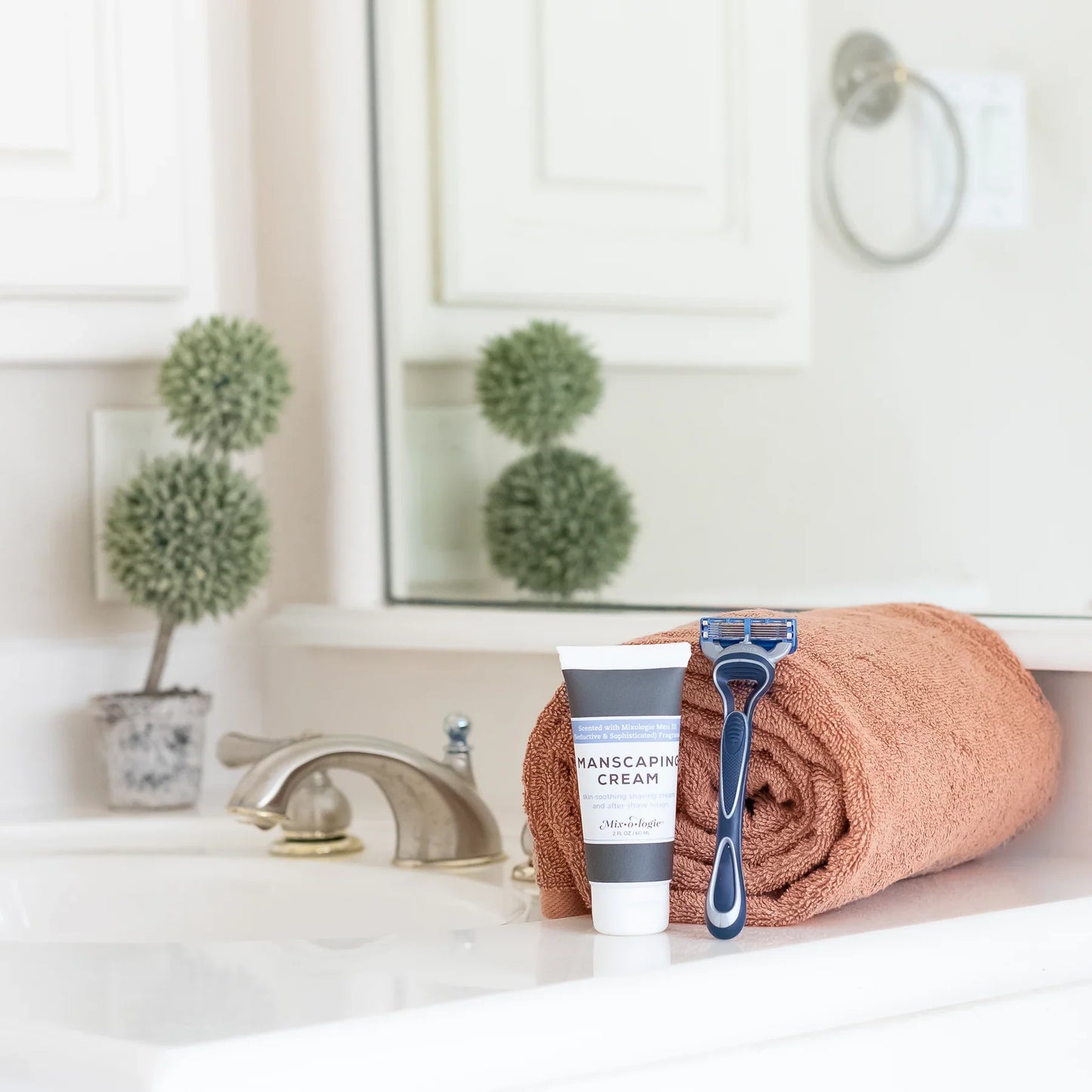 A blue and black disposable five-blade razor resting on a rolled terracotta towel with mixologie manscaping cream shave lotion sent iii