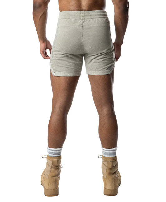 Rear view of a person wearing sage green Nasty Pig Traverse rugby shorts, striped socks, and tan boots.