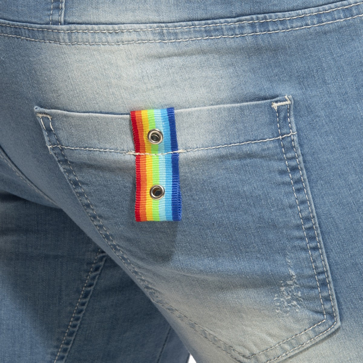 Rainbow tape jean short featuring a rainbow-striped ribbon button with metallic grommets on a denim pocket