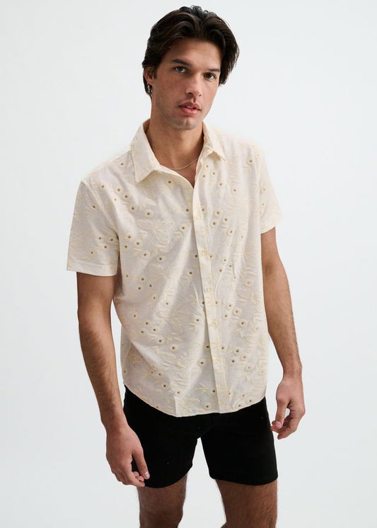 A short-sleeve button-down shirt in vanilla white with an all-over embroidered eyelet and floral print pattern.