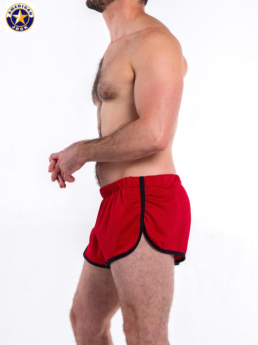 Red gym jogging shorts with black trim featuring an elastic waistband shown on a model from the side by AMERICAN JOCK