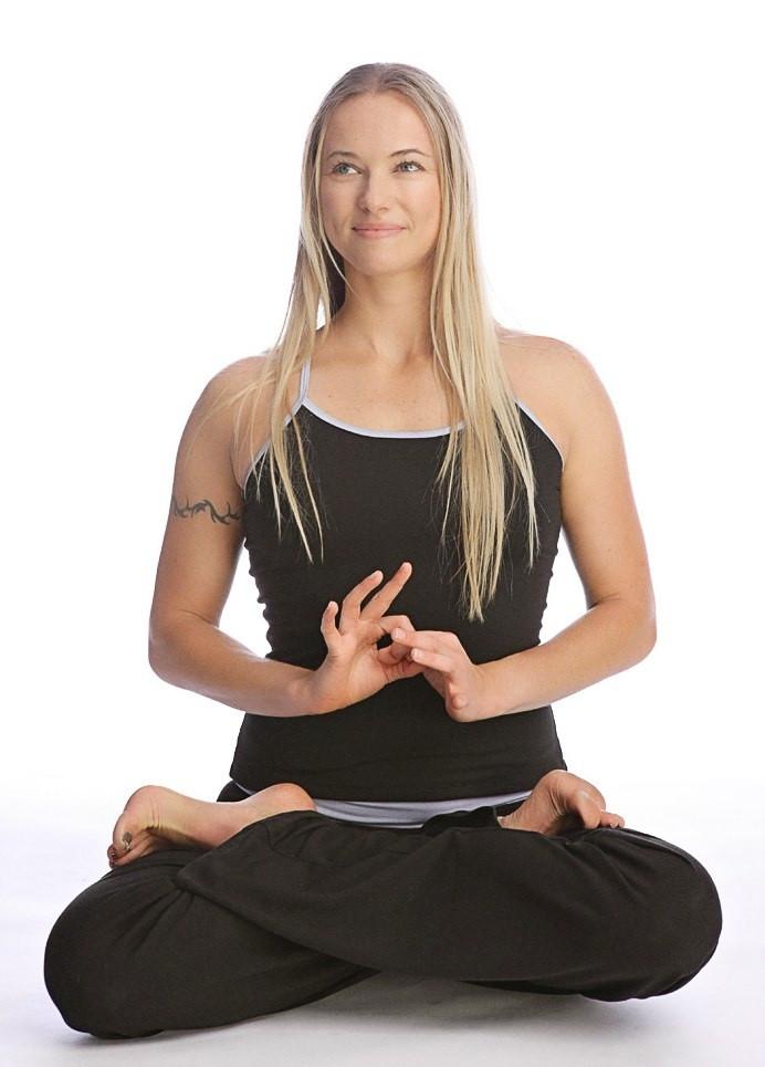 Woman wearing a black sustain yoga halter tank top sitting cross-legged with hands forming a mudra