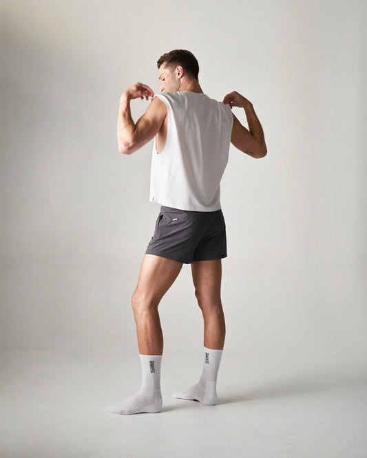 Rear three-quarter view of a white muscle tank top paired with dark grey shorts and white socks.
