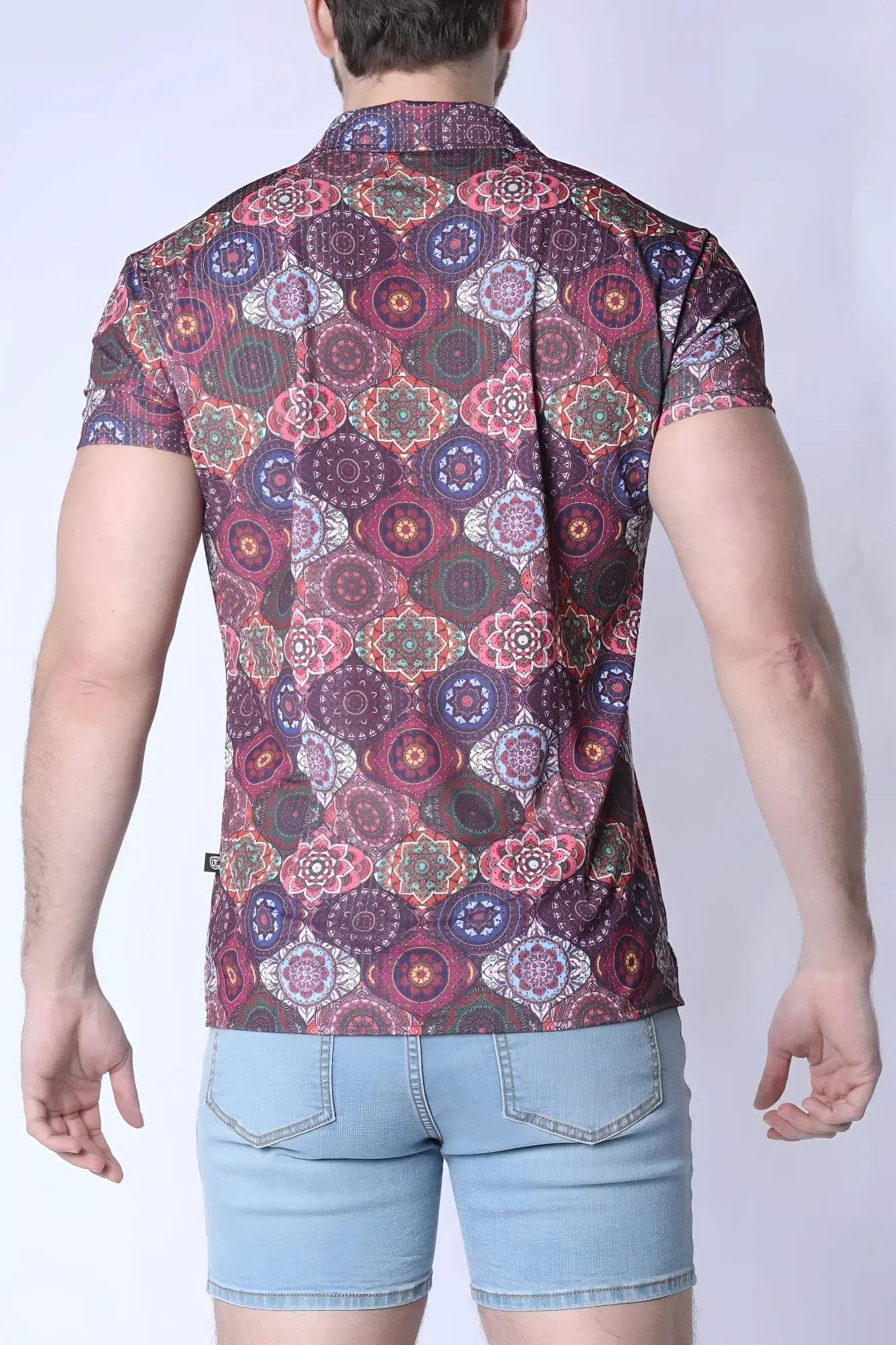 A man wearing a balboa button down shirt with a colorful purple pink and green mandala pattern on dark maroon fabric