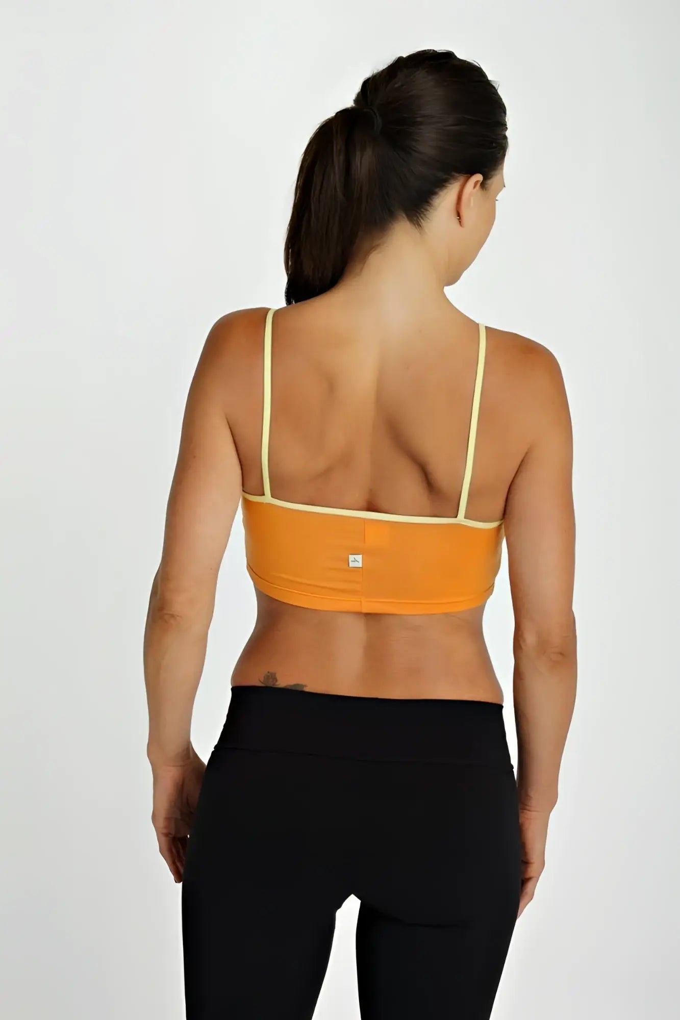Orange sports bra top tangerine with thin yellow straps and a small brand logo visible on the back side