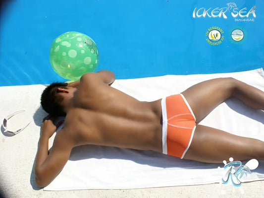 Orange swim trunks with white contrast trim lying on a towel beside a pool from icker sea swimwear collection