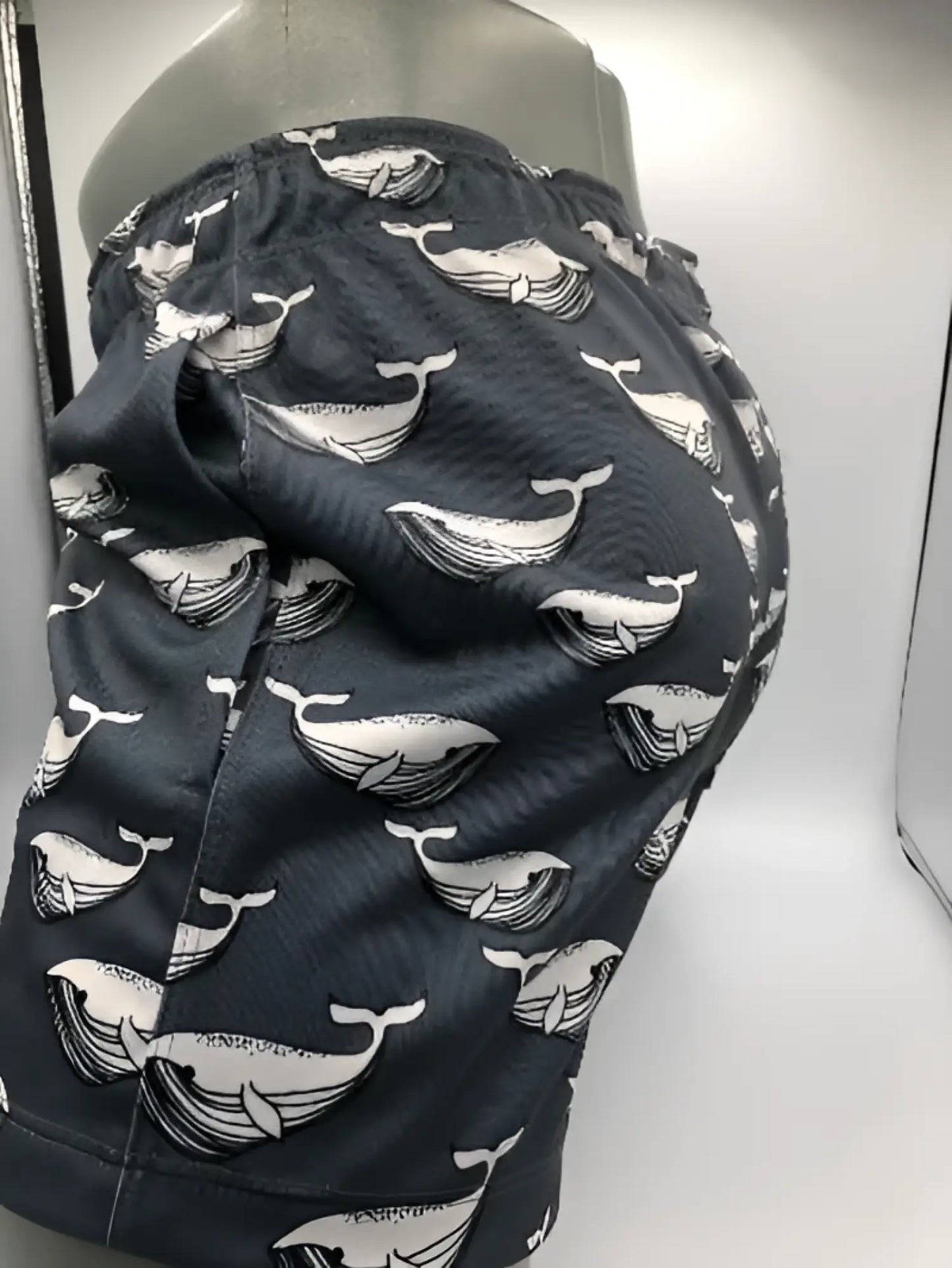 Dark gray moby dick shorts with a repeating white whale pattern ideal for swimwear and beach use
