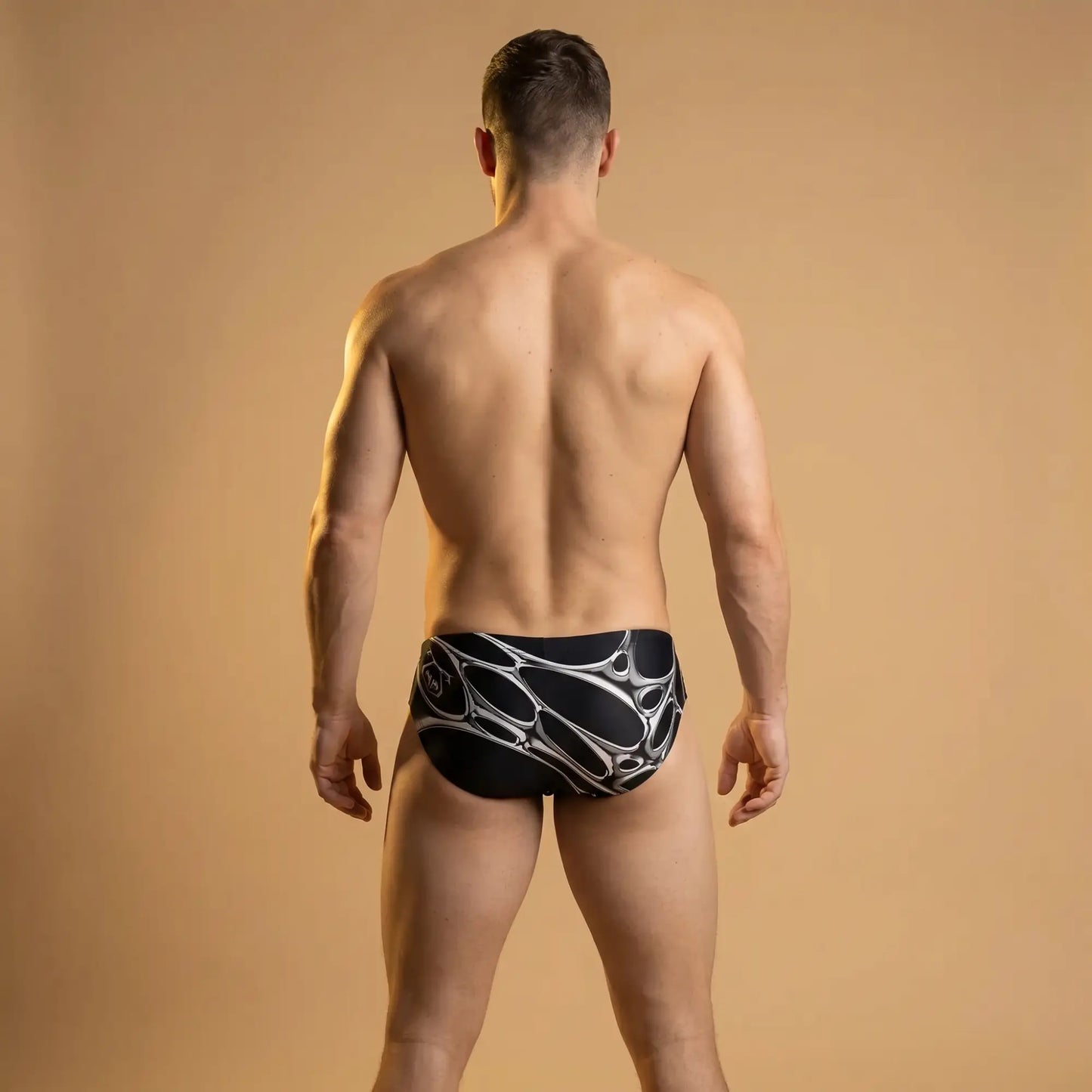 Black briefs featuring a silver 3D liquid metal chrome graphic pattern on a muscular model from the back.