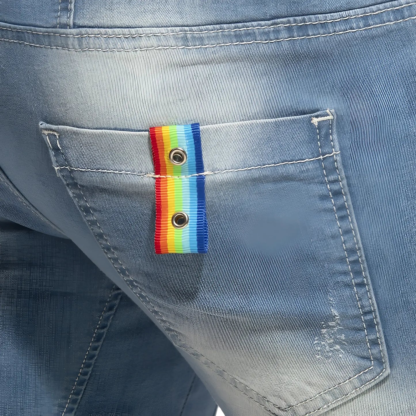 Rainbow tape jean short featuring a rainbow-striped ribbon button with metallic grommets on a denim pocket