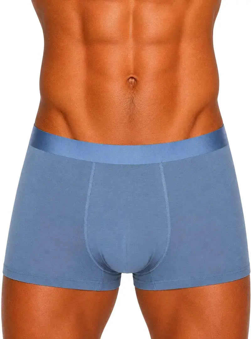 Muscular man standing against plain background wearing blue cotton boxer briefs.