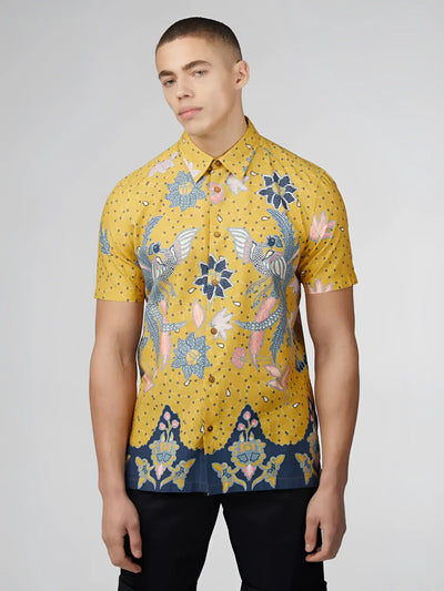 A man wears a yellow short-sleeve shirt with blue patterned batik motifs.