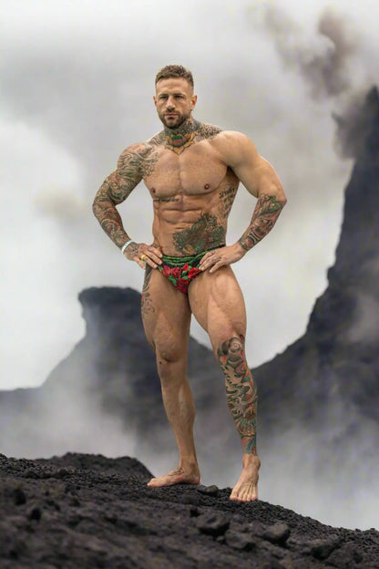 Men's swim briefs in red with rose print featuring a snug fit shown by a model against a volcanic backdrop by Maris Equi