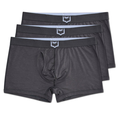 Dark gray men’s sheath 2.1 dual pouch trunks with a white shield logo on the waistband in a 3 pack bundle