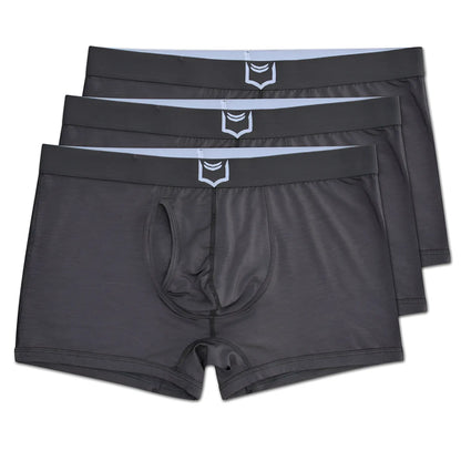 Dark gray men’s sheath 2.1 dual pouch trunks with a white shield logo on the waistband in a 3 pack bundle
