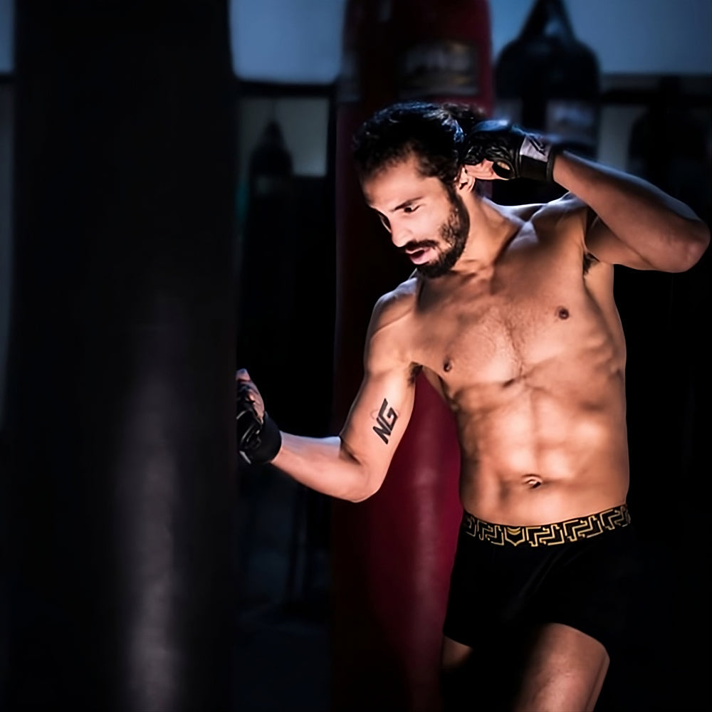 A man wearing black sheath 3.0 modal men’s no-fly boxer briefs with gold greek key pattern waistband and black boxing gloves