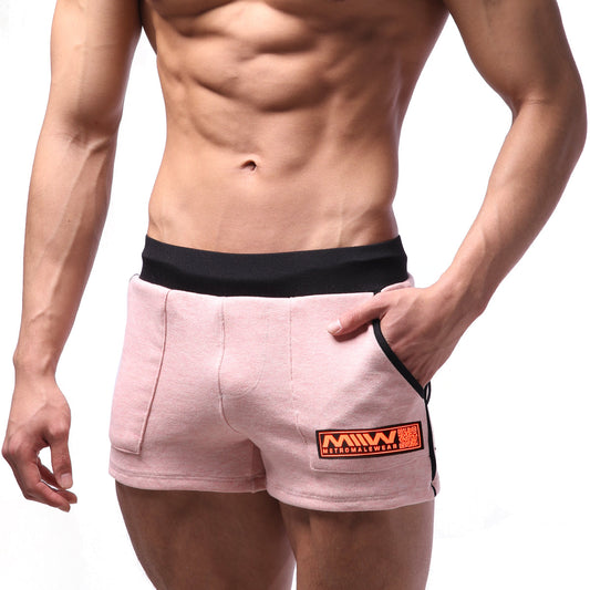 Pink cotton athletic shorts with black waistband and side trim featuring an orange logo patch on front pocket