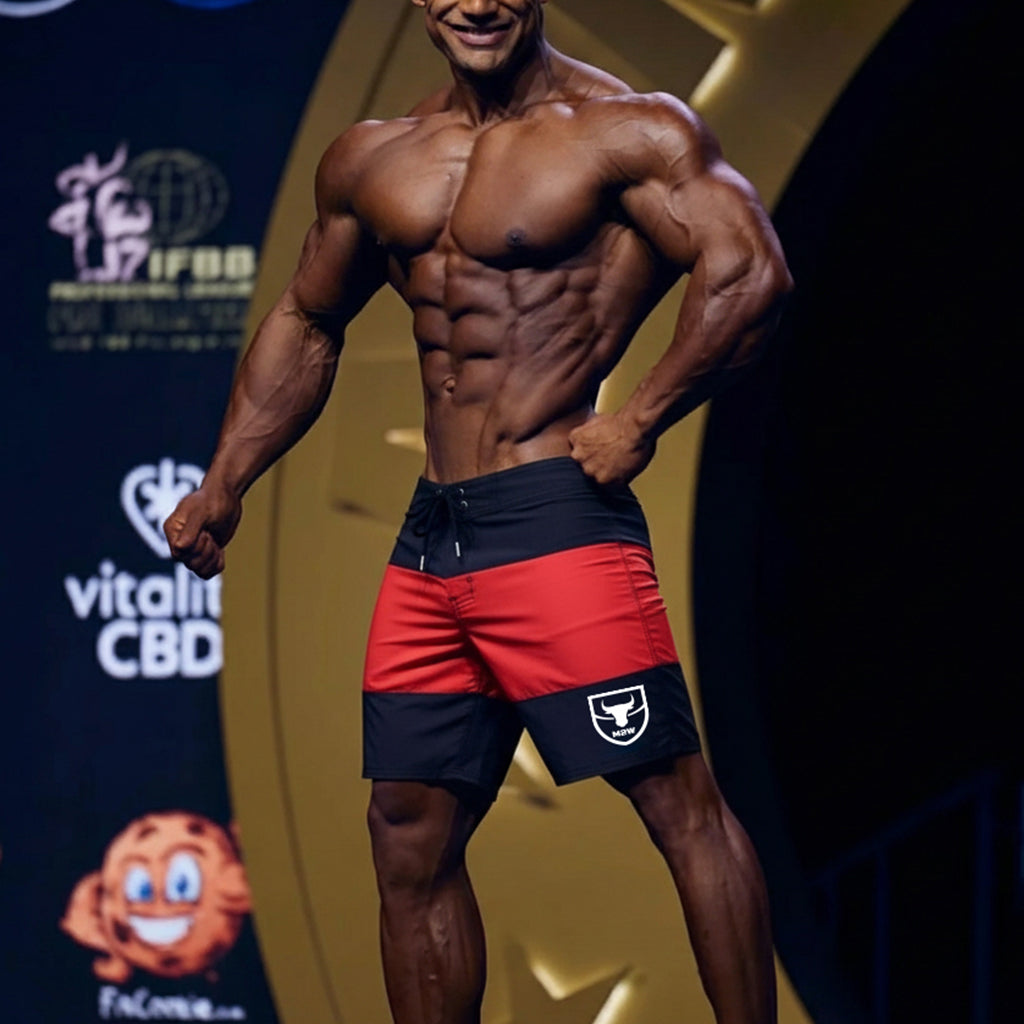 A muscular man wearing red and black MetroMaleWear physique board shorts with a white bull logo on the left leg