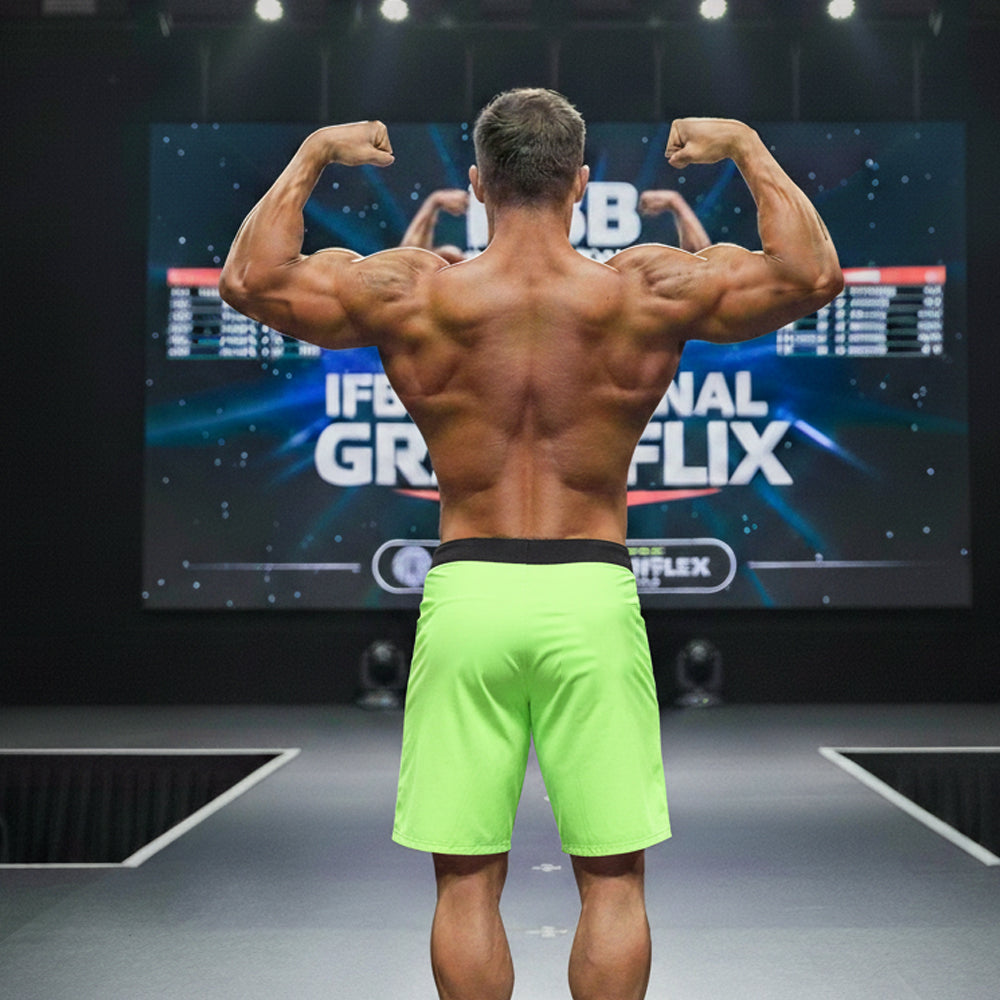 A muscular man in neon green metroMalewear physique board shorts with black waistband on stage bodybuilding competition