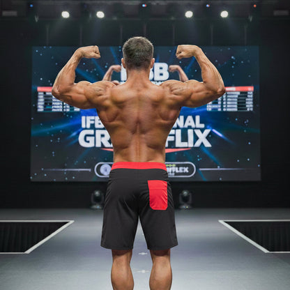 A muscular man wearing metroMalewear physique board shorts in black with a red waistband and red pocket detailing