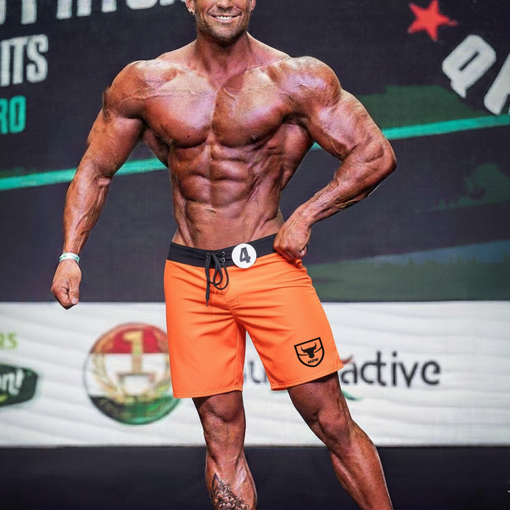 Orange athletic shorts with black waistband and drawstring featuring small shield logo on lower right leg from metromalewear