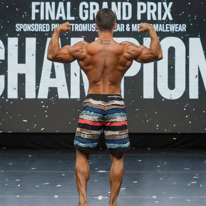A muscular man wearing metroMalewear metallure tiger physique board shorts in blue red beige camouflage pattern