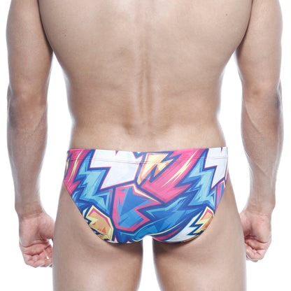 MetroMalewear Vasco hip brief swim trunks with vibrant pink blue and yellow lightning bolt graffiti pattern on white base