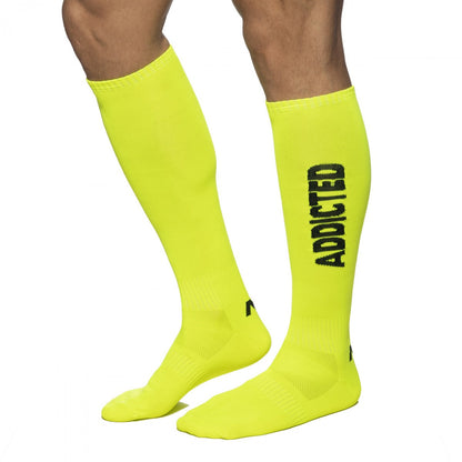 Bright neon yellow knee-high socks with bold black addicted lettering on the side for streetwear style