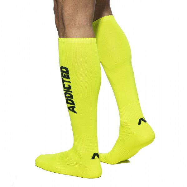 Bright neon yellow knee-high ADDICTED socks with black lettering and a small logo on the foot