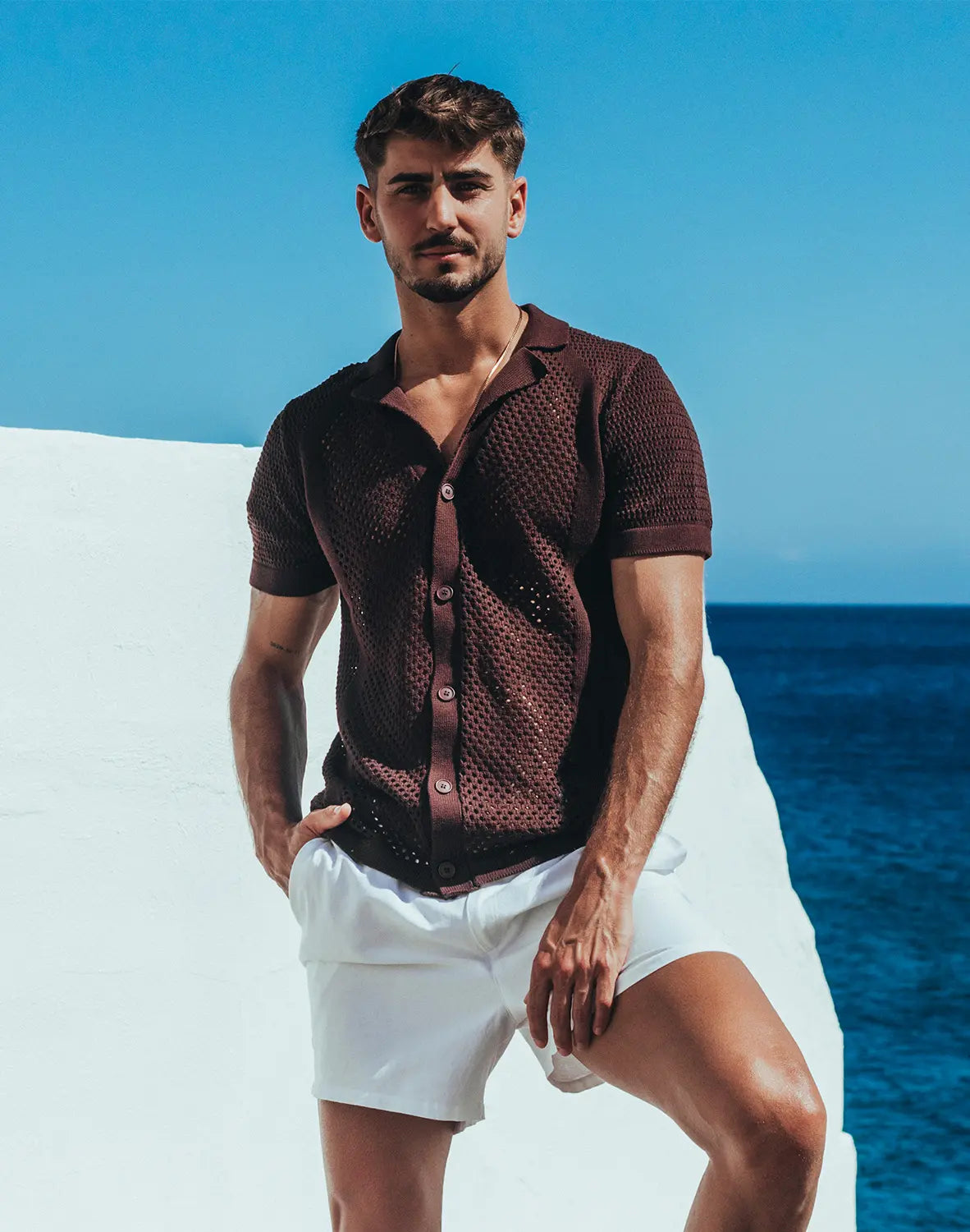A man wearing an amafi knit shirt dark brown short sleeved button up with open collar and textured fabric