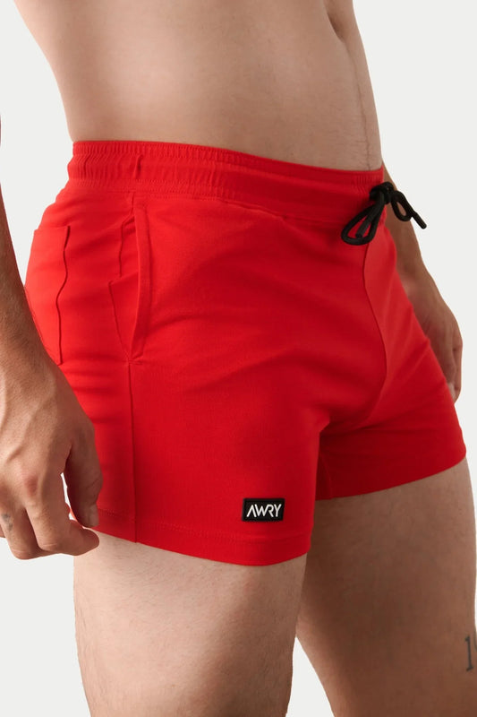 Bright red gym shorts featuring a black drawstring and small black and white AWRY logo tag on the left hem.