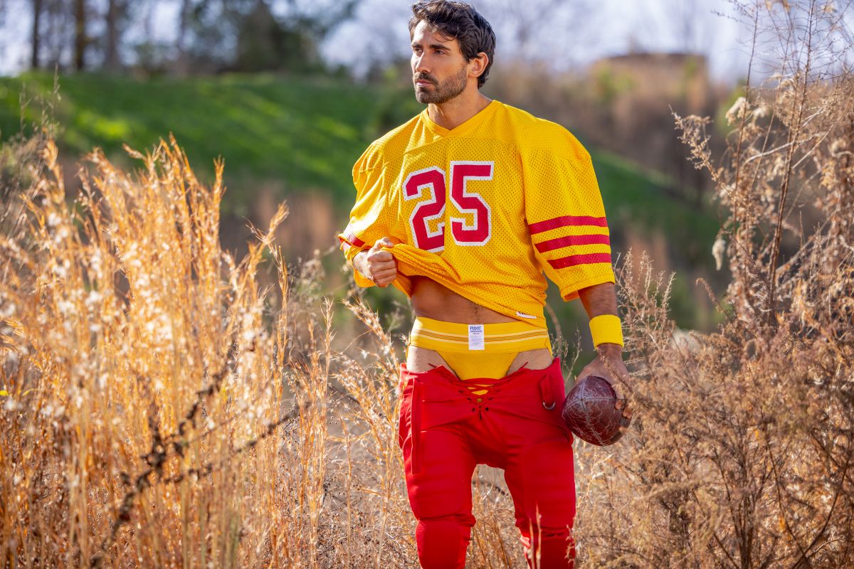 A man wearing a BIKE Athletic BAS306 original number 10 yellow jockstrap with a vibrant yellow and red football jersey and pants