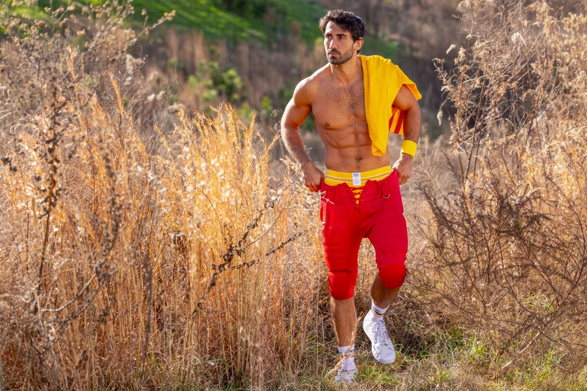 A muscular man wearing BIKE athletic BAS306 original number 10 yellow jockstrap with red shorts and white sneakers