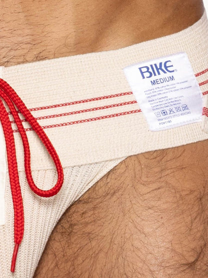 Beige bike brand swim trunks with red drawstring and trim paired with vintage cream bike athletic lace-up jockstrap