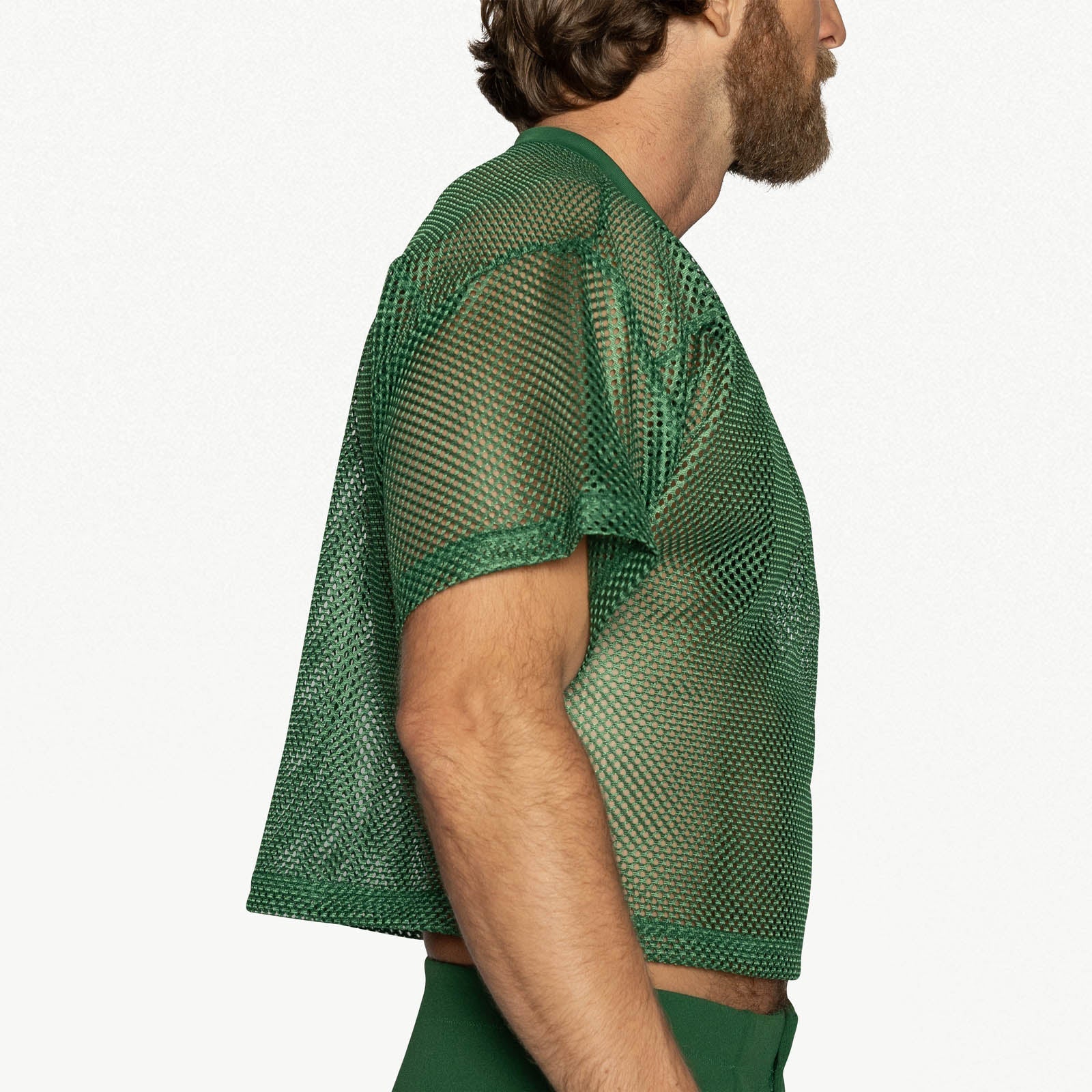 Side profile of a person wearing a green mesh practice jersey with short sleeves against a white background.