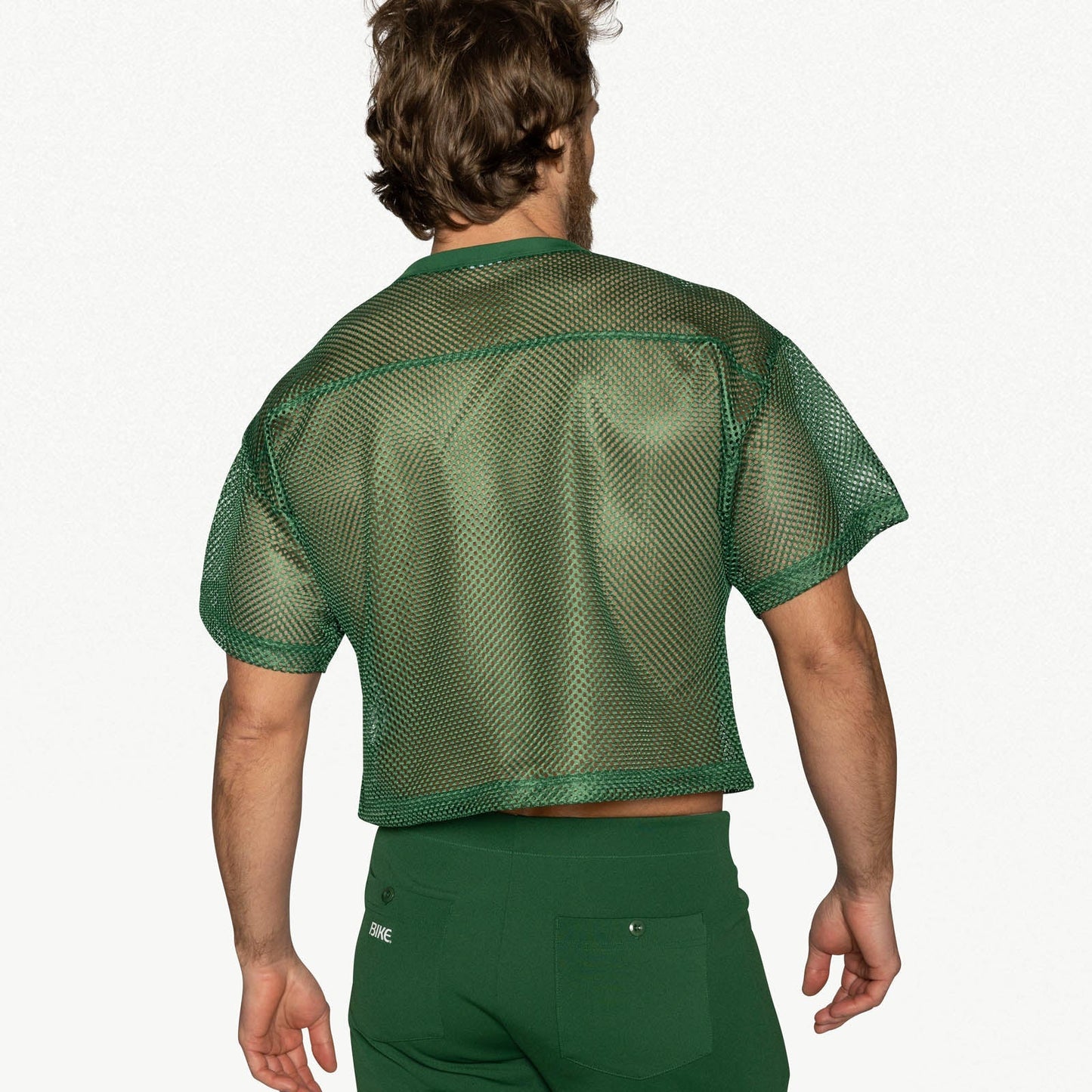 Back view of a person wearing a green mesh practice jersey and matching green pants.