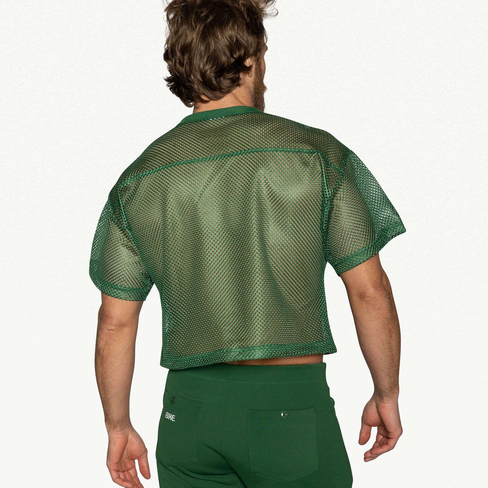 Back view of a person wearing a green mesh practice jersey and matching green pants.