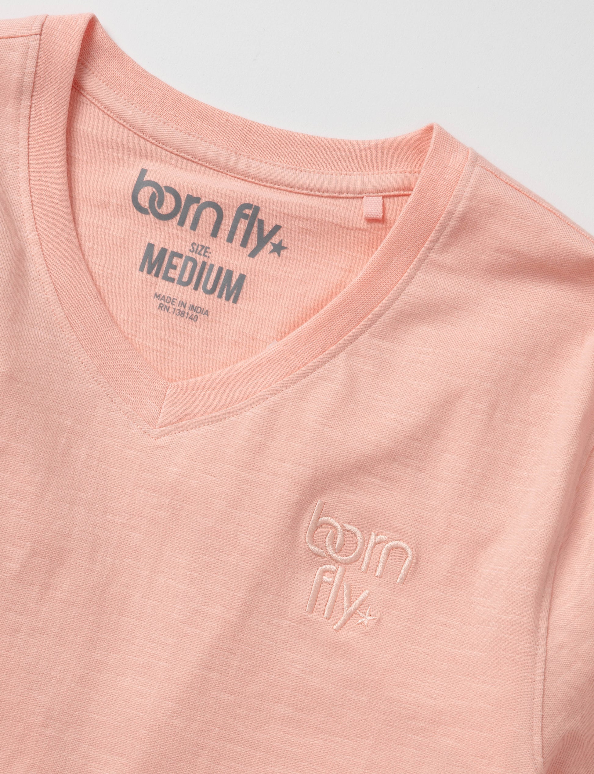 A soft peach-colored cotton born fly v-neck tee with subtle embroidered logo and brand tag at the neckline