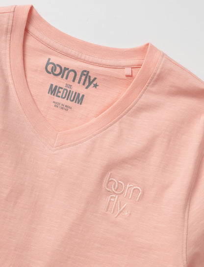 A soft peach-colored cotton born fly v-neck tee with subtle embroidered logo and brand tag at the neckline
