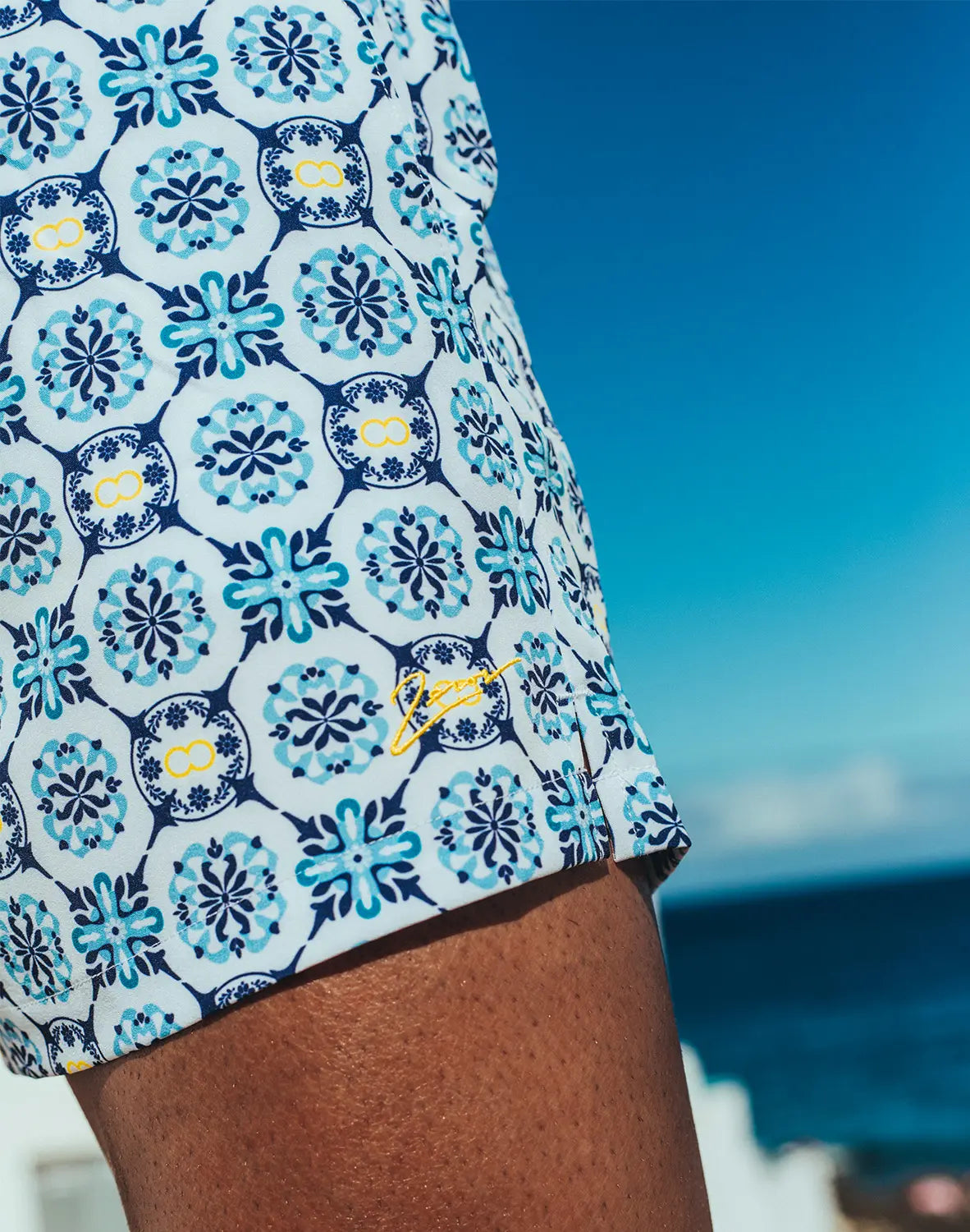 Byron swim short Mykonos print white swim trunks with teal navy floral tile pattern yellow accents and side logo