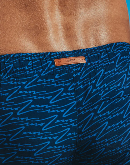 Dark blue Byron swim shorts with light blue abstract line print and tan leather brand tag for casual beachwear
