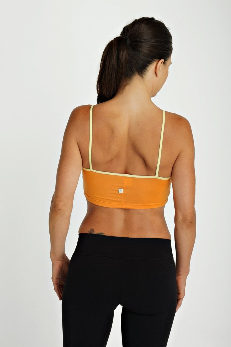 Orange sports bra top tangerine with thin yellow straps and a small brand logo visible on the back side