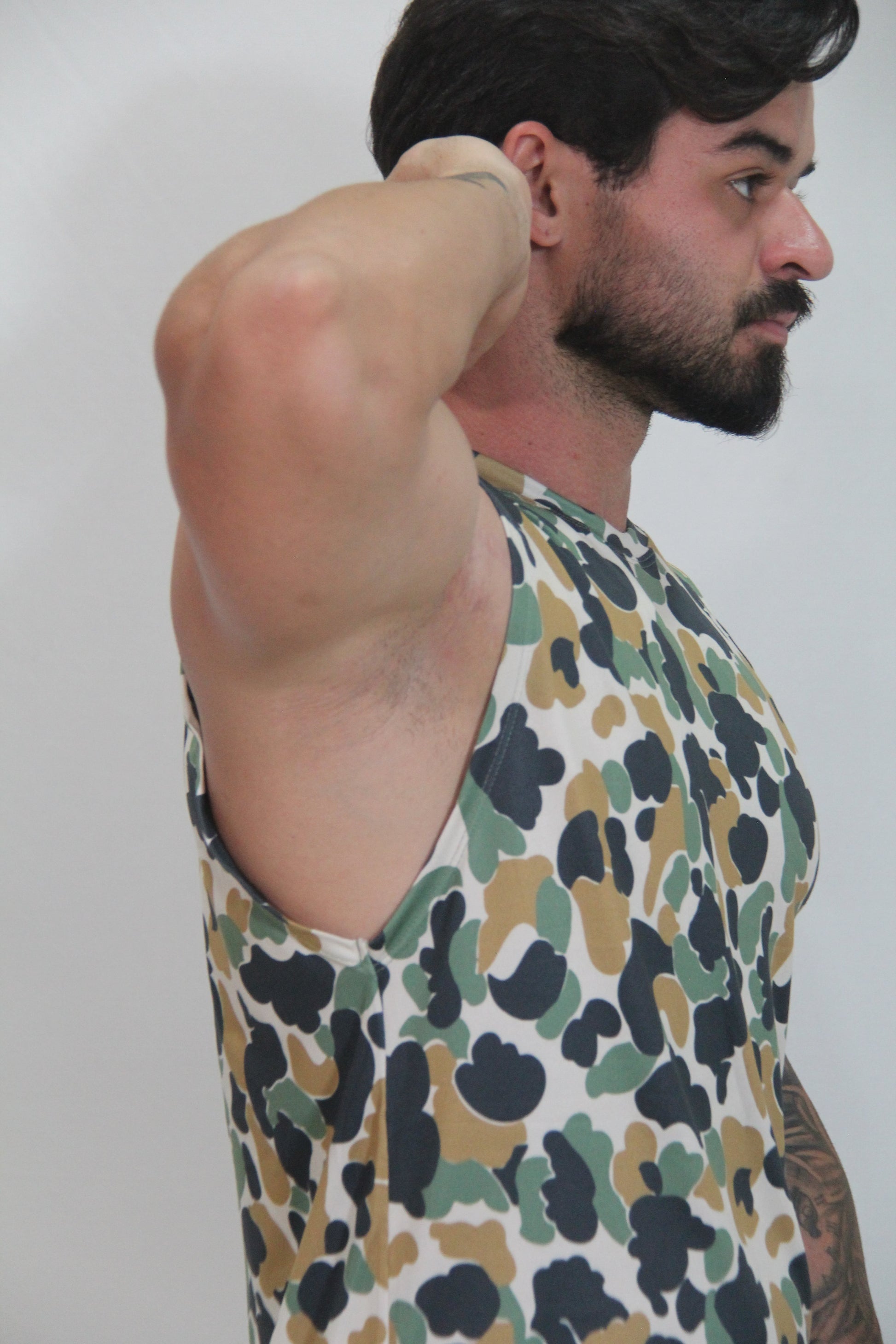 A man wearing a camouflage open arm tank with black green and tan splotches on a white base