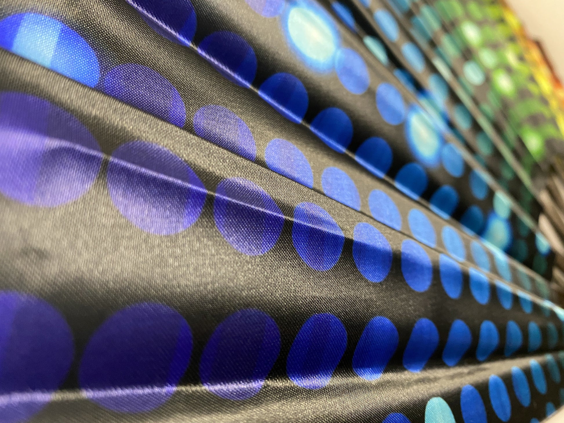 Black fabric from clack fans with overlapping blue circles pattern in varying shades smooth texture and subtle sheen