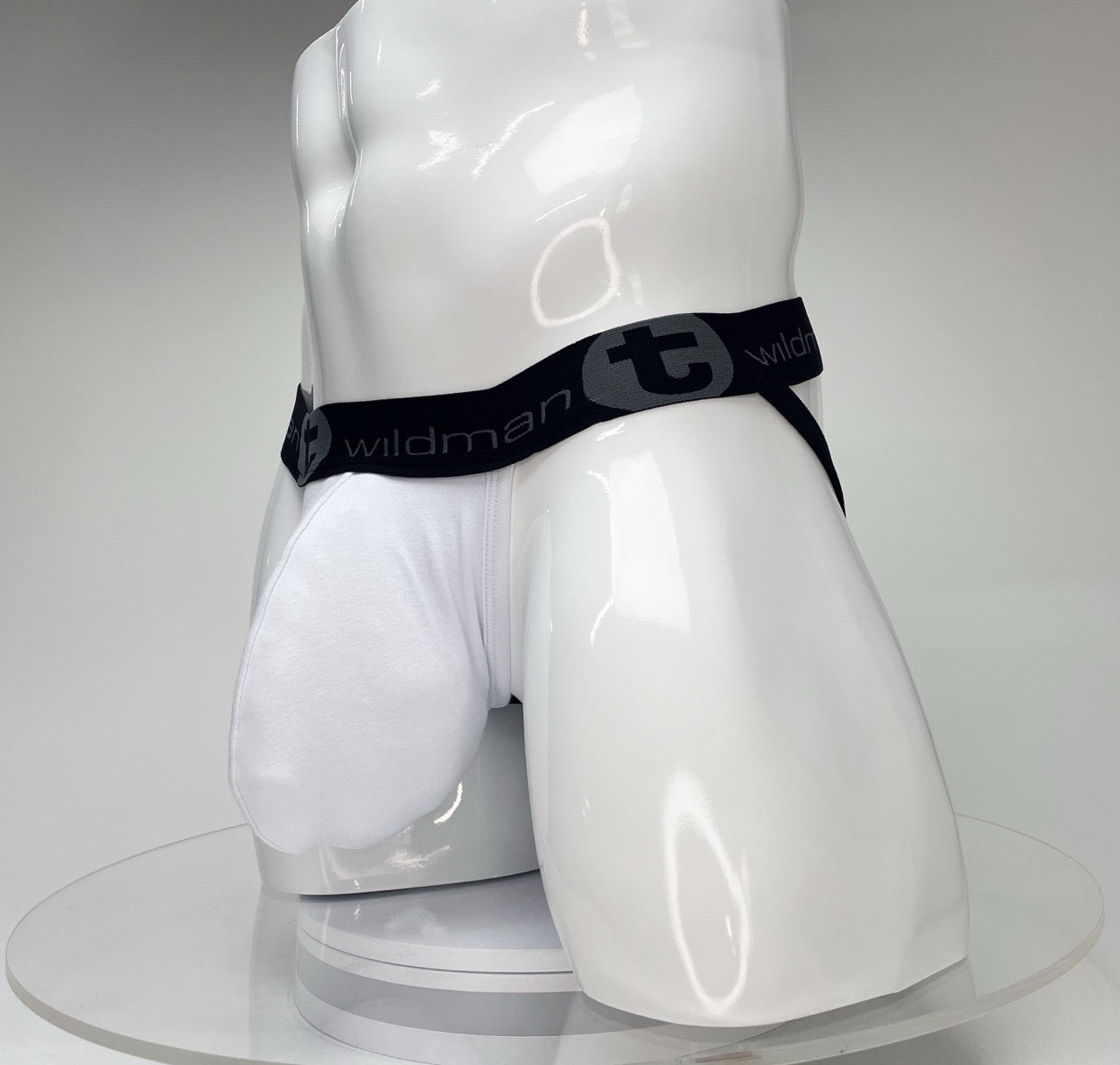 White WildmanT jockstrap with a large front pouch and a black branded elastic waistband on a white mannequin torso.