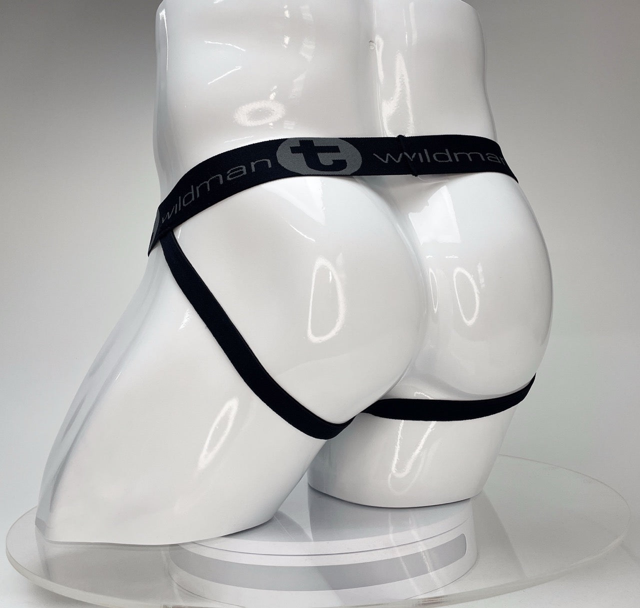 White jockstrap on a white mannequin featuring a black elastic waistband with "WildmanT" logo and leg straps.